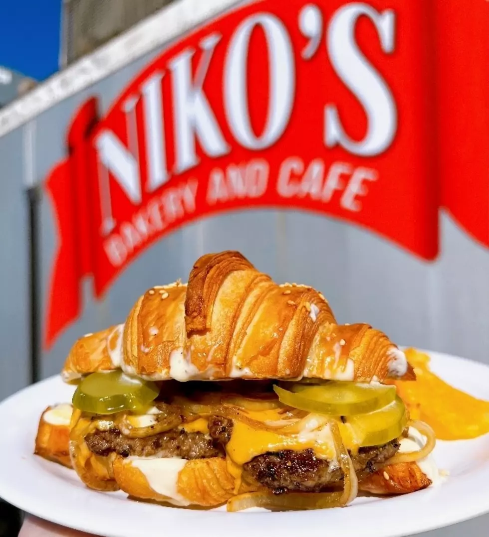 Croissant sandwich held in front of Niko’s Bakery & Cafe
